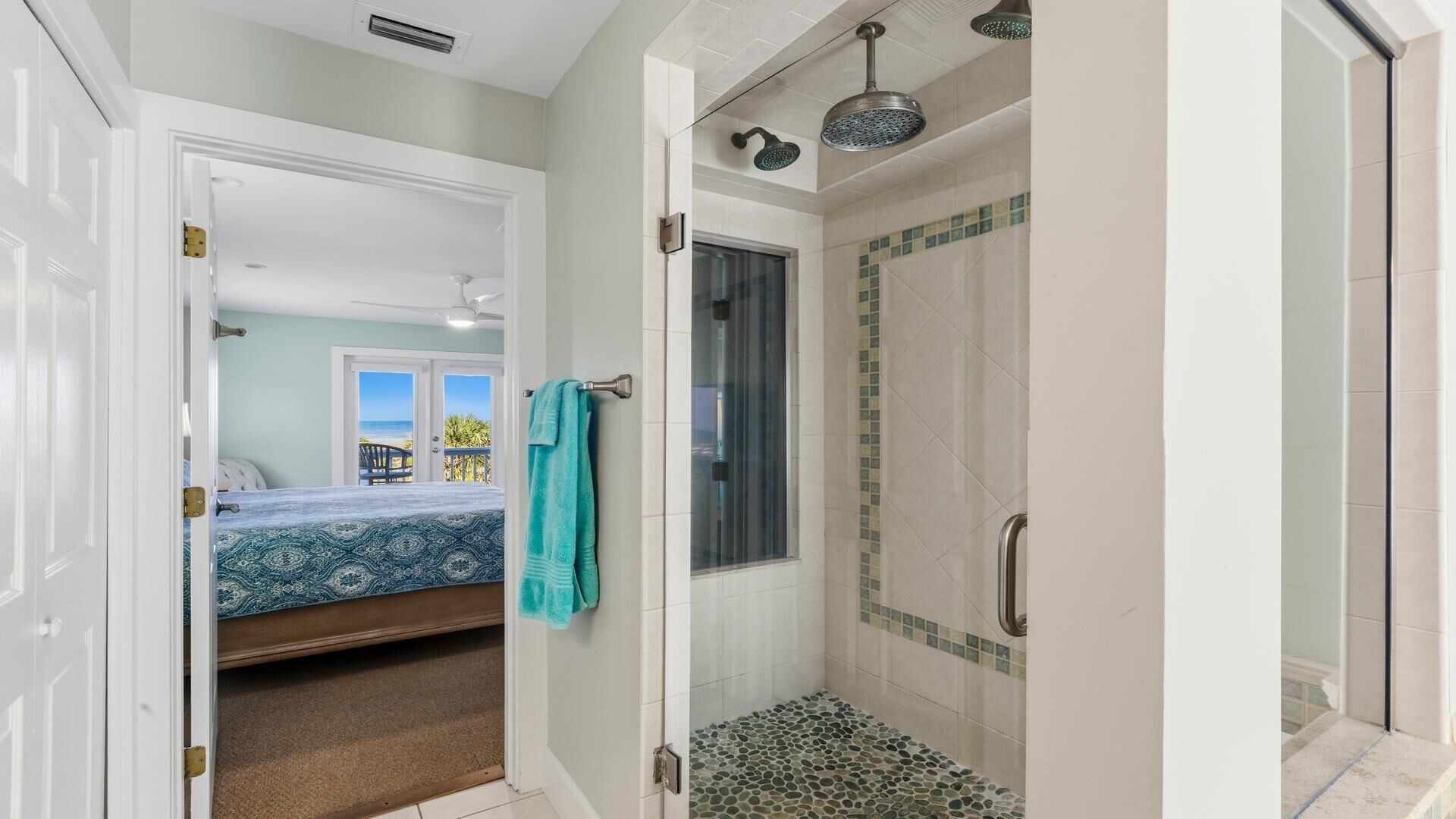 Une salle de bain avec douche, une porte donnant sur une chambre, et vue sur la plage.