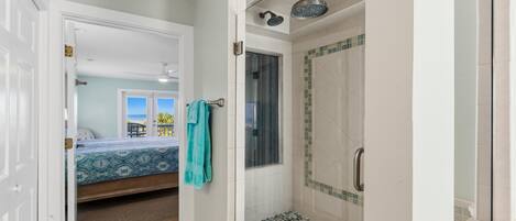Une salle de bain avec douche, une porte donnant sur une chambre, et vue sur la plage.