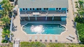 Vue aérienne d’un hôtel avec une piscine, des chaises longues et une terrasse couverte.