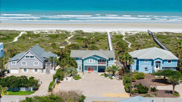 Una propiedad frente al mar con tres casas, un camino de entrada pavimentado y un paseo marítimo que lleva a la playa.