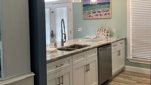 A kitchen with white cabinets, a marble countertop, a stainless steel dishwasher, and pendant lights. - Relaxing beach retreat steps away to beach, pools, hot tub tennis/pickleball! (Destin)