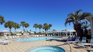 A swimming pool with lounge chairs and palm trees. - Relaxing beach retreat steps away to beach, pools, hot tub tennis/pickleball! (Destin)