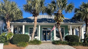 A two-story building with a covered porch, palm trees, and a brick pathway leading to the entrance. - Relaxing beach retreat steps away to beach, pools, hot tub tennis/pickleball! (Destin)