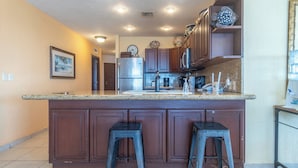 A kitchen with dark wooden cabinets, a granite countertop, stainless steel appliances, and two bar stools.