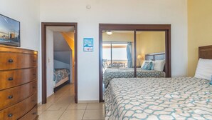A hotel room with a bed, a dresser, and a view of the beach through a sliding door.