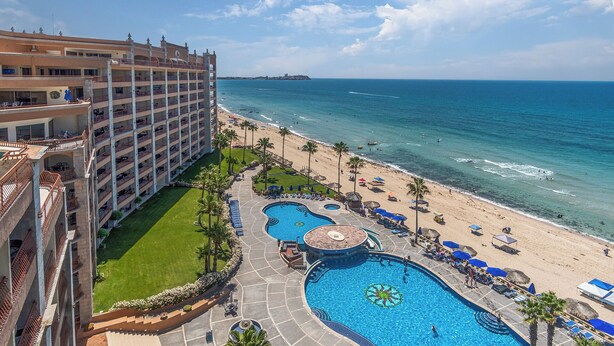 A hotel with multiple floors, a pool area with two swimming pools, a beach, and the ocean.