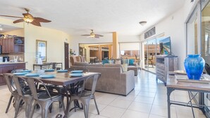A spacious living area with a dining table, chairs, a sofa, and a large window offering a view of the outdoors.
