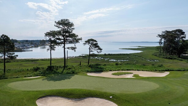 A golf course with bunkers, trees, and a body of water in the background.