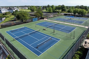 Complejo de canchas de tenis con múltiples canchas, cercas y una masa de agua al fondo.