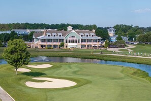 A golf course with a clubhouse featuring multiple levels and a pond. - 22096 S Preservation Drive (Millsboro)