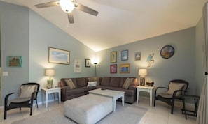 A living room with a ceiling fan, a sofa set, a coffee table, and framed artwork on the walls.