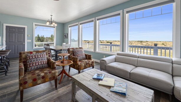 A spacious living room with a large window overlooking a beach, a dining area with a table and chairs, and a cozy seating area with a sofa and armchairs. - PICKLEBALL, NEW HOT TUB, Ocean View, Playset (SV2) (Long Beach)