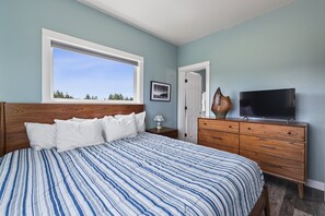 Une chambre à coucher avec un grand lit, une commode en bois, un téléviseur et une fenêtre donnant sur les arbres.