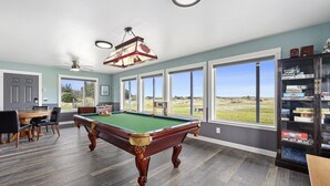 A pool table in a room with large windows, a ceiling fan, and a bookshelf with puzzle games. - PICKLEBALL, NEW HOT TUB, Ocean View, Playset (SV2) (Long Beach)