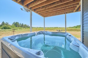 Un bain à remous installé sous une pergola en bois, offrant une vue dégagée sur un champ verdoyant et des arbres.