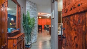 A hallway with a wooden door, a stone wall, a plant, a dining area with a table and chairs, and a ceiling fan. - Sonoran Sun W-510 Sunny Charmed Life Adorable Oceanfront Condo (Puerto Penasco)