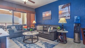A living room with a blue wall, a leather sofa, a coffee table, and a water dispenser. - Sonoran Sun W-510 Sunny Charmed Life Adorable Oceanfront Condo (Puerto Penasco)