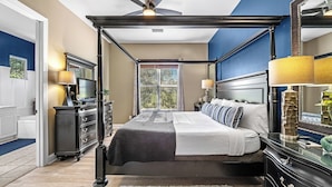 Ein Bett mit Himmelbett, Deckenventilator, großes Fenster mit Jalousien, eine Kommode und ein Spiegel.