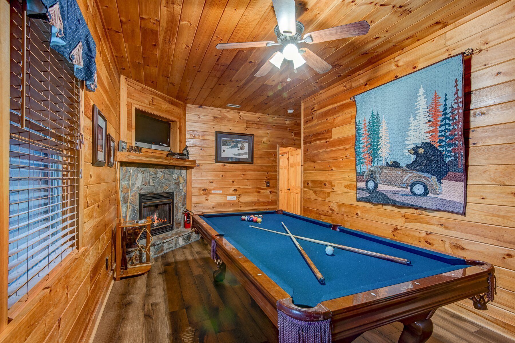 A wooden cabin interior with a pool table, a fireplace, and a ceiling fan.