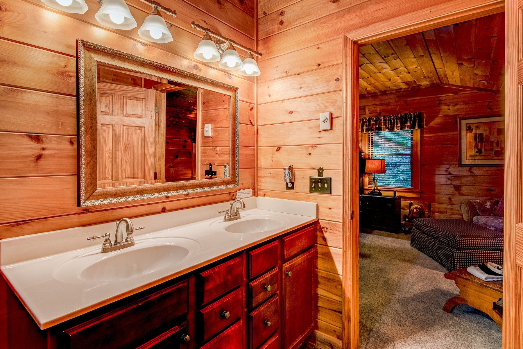 Baño de cabaña de madera con dos lavabos, un espejo grande y techo de madera.
