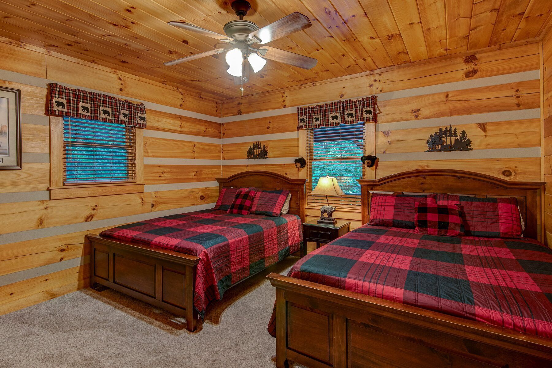 A cabin-style bedroom with two wooden beds, a ceiling fan, and plaid curtains.