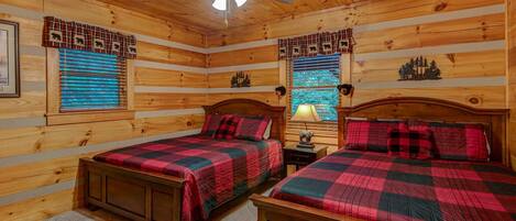 A cabin-style bedroom with two wooden beds, a ceiling fan, and plaid curtains.