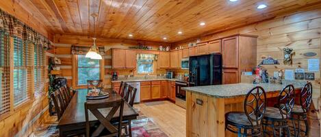 A wooden cabin interior with a dining area, kitchen, and bar seating.