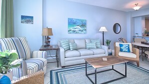 Una sala de estar con sofá, sillón, mesa de centro, lámpara y cuadros en la pared.