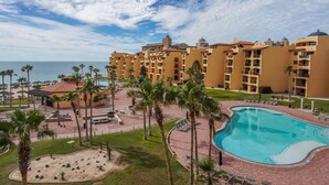 A resort with a swimming pool, palm trees, and a view of the ocean.
