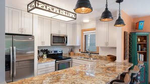 Una cucina con mobili bianchi, elettrodomestici in acciaio inossidabile, un piano di lavoro in granito e illuminazione a sospensione.
