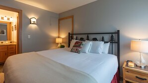 Un letto rifatto con lenzuola bianche, un comodino con una lampada e uno specchio fissato al muro.