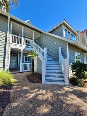 A two-story house with a front porch, a staircase, and a small palm tree.
