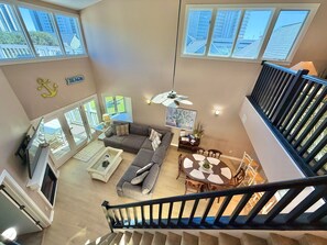 A spacious living area with a sofa, coffee table, and dining table, a staircase, and large windows offering views of buildings.