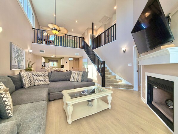 A spacious living area with a sofa, coffee table, and a fireplace. A staircase leads to an upper level with a balcony.