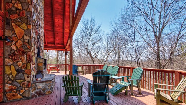 Una terraza de madera con sillas Adirondack, un muro de piedra y una barandilla roja.