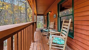 Eine hölzerne Veranda mit Geländer, zwei Schaukelstühle und ein Fenster mit Blick auf Bäume.