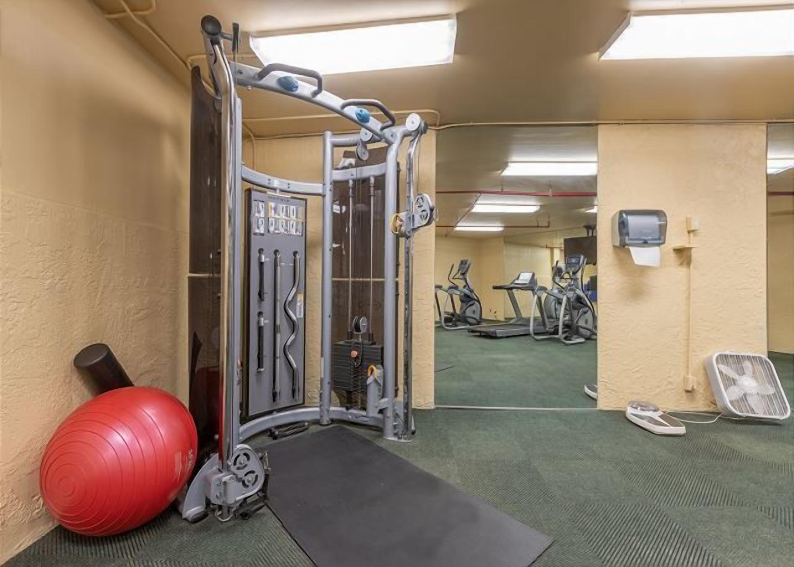 Een sportschool met een pull-up bar, een rode fitnessbal en een spiegel die loopbanden en andere apparatuur reflecteert.