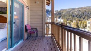 Un'elegante terrazza in legno con una porta vetrata che conduce a una camera da letto, una poltrona rossa e vista su maestose montagne innevate.