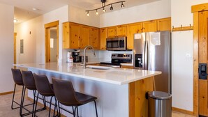 Una cucina moderna con mobili impiallacciati in legno, elettrodomestici in acciaio inossidabile, una grande isola con sgabelli da bar e un cestino.