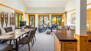 Amplia sala de estar con una gran mesa de madera, asientos cómodos y ventanas amplias con vistas al exterior.