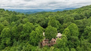 A multi-story building surrounded by dense forest with a view of distant mountains. - Stags Leap in Yonahlossee  Pool Table, Indoor Pool, Tennis Courts (Boone)