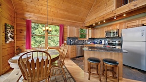 A wooden cabin interior with a dining area, kitchen, and bar seating. - 3 Peaks Lodge - Charming Pet Friendly Cabin with great views, hot tub and pool table! (Vilas)