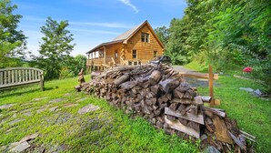 A wooden cabin with a porch, surrounded by a stone pathway and a pile of firewood. - 3 Peaks Lodge - Charming Pet Friendly Cabin with great views, hot tub and pool table! (Vilas)