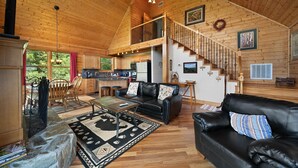 A spacious living area with a wooden ceiling, a black leather sofa, a dining table, and a staircase leading to an upper level. - 3 Peaks Lodge - Charming Pet Friendly Cabin with great views, hot tub and pool table! (Vilas)