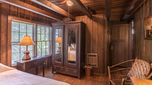 Ein rustikaler Holzraum mit einem großen Schrank, einem Bett mit gemustertem Überwurf, einem Sessel und einem Fenster mit Jalousien.