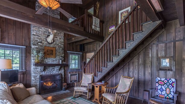 Ein rustikales Interieur mit Kamin aus Stein, einer Holztreppe und einer gemütlichen Sitzecke.