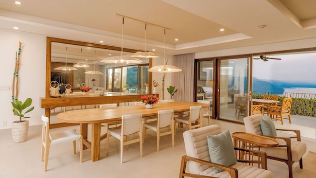 A spacious dining area with a large wooden table and chairs, a modern chandelier, and a large mirror.