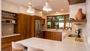 A modern kitchen with wooden cabinets, a stainless steel refrigerator, and pendant lighting.
