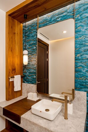 A bathroom with a wooden vanity, a white sink with gold fixtures, and a mirror with a blue marble backsplash.
