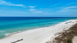 Une plage avec une jetée qui s’avance dans l’océan, un rivage sablonneux et un ciel bleu clair.